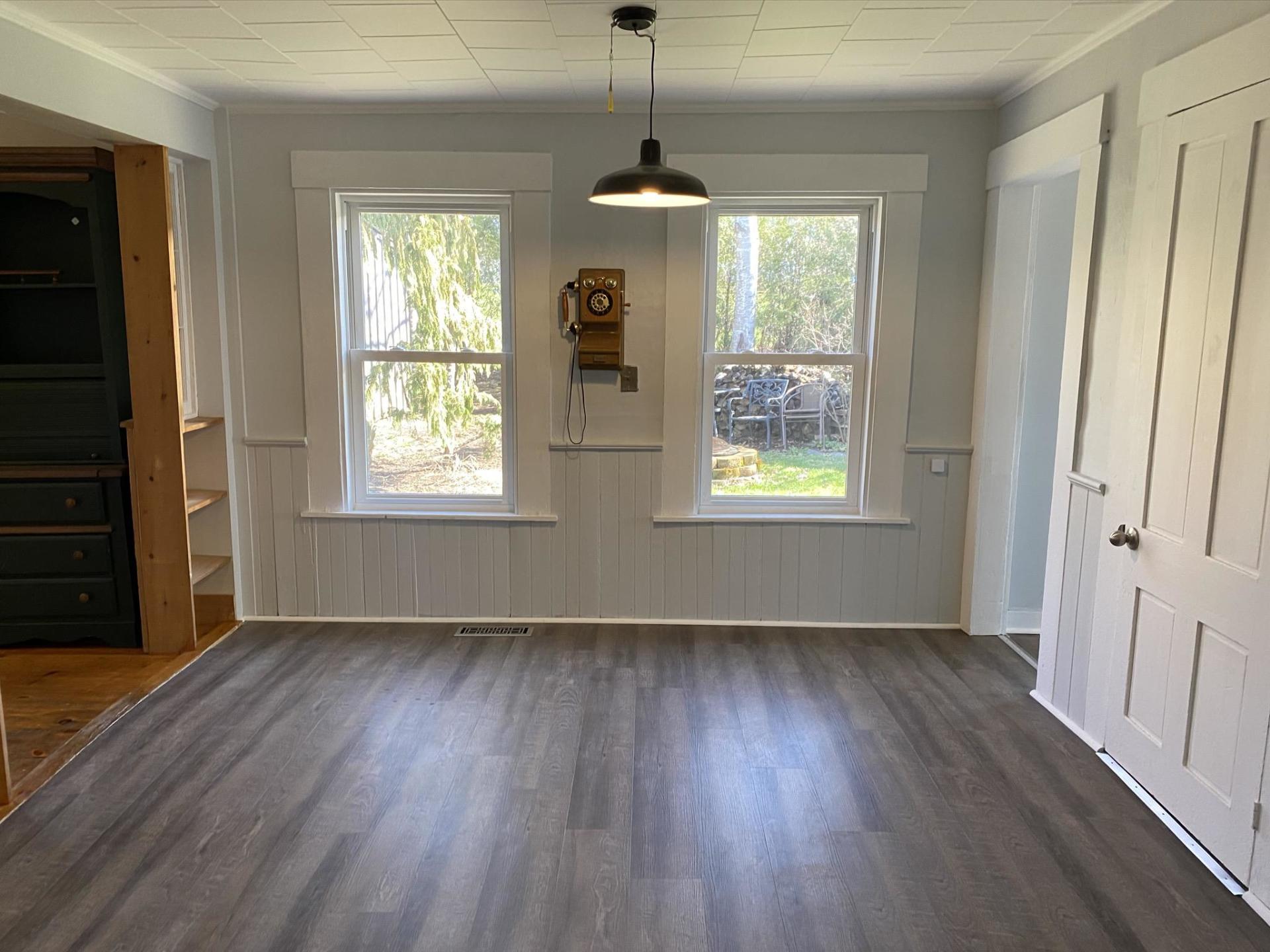 Empty room with gray flooring, two windows, and a hanging light fixture.