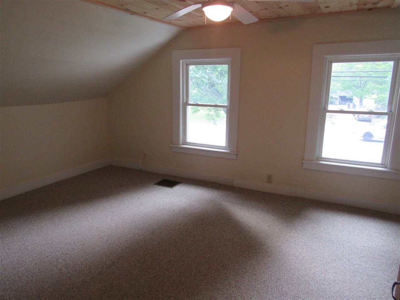 Empty bedroom with tan walls, carpet, two windows, and a ceiling fan.