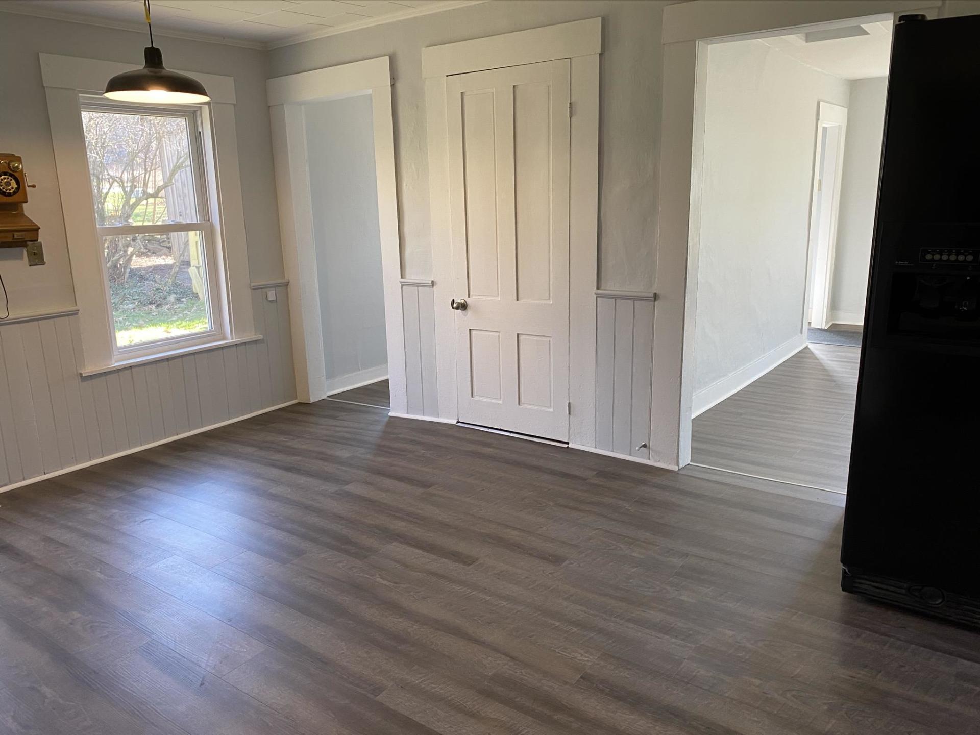Room with gray wood-look flooring. White-trimmed doorways and a closet. A window lets in sunlight.