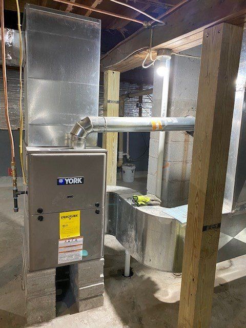A new York furnace and ductwork installed in a basement, with wooden beams and concrete supports.