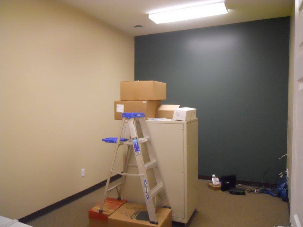 A room with a ladder, cardboard boxes, and a beige filing cabinet against a dark green wall.
