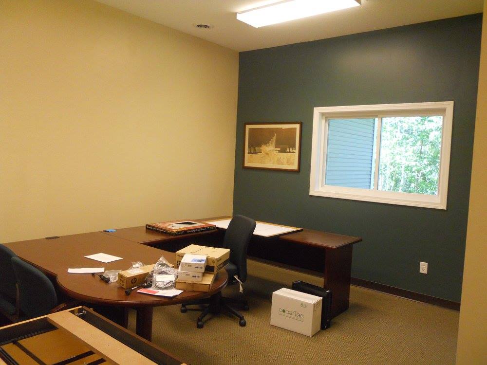 Empty office with desk, chair, window, framed art, and cardboard box on the floor.