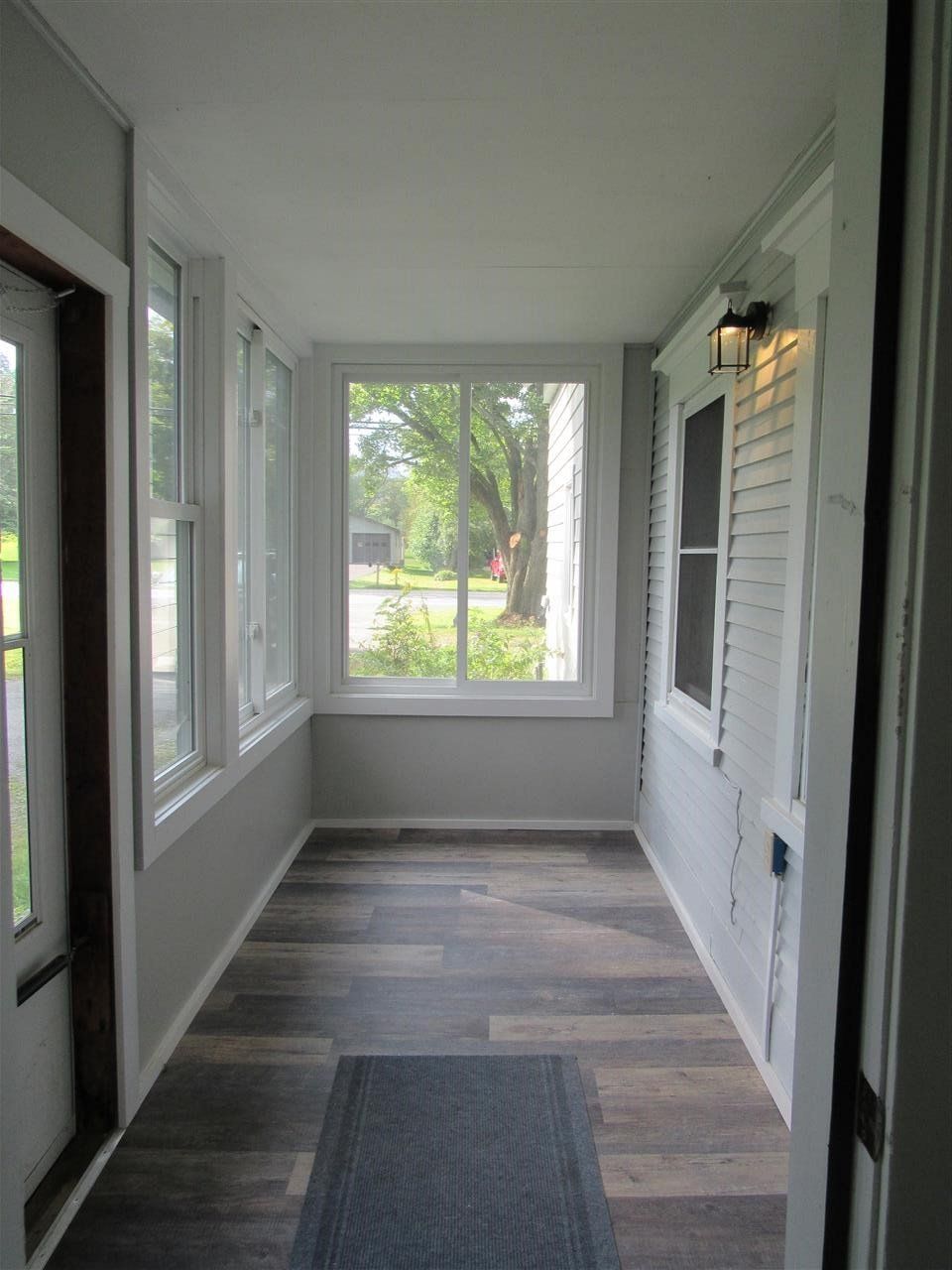 Sunroom with white walls, windows, and wood-look flooring. A small rug is on the floor.