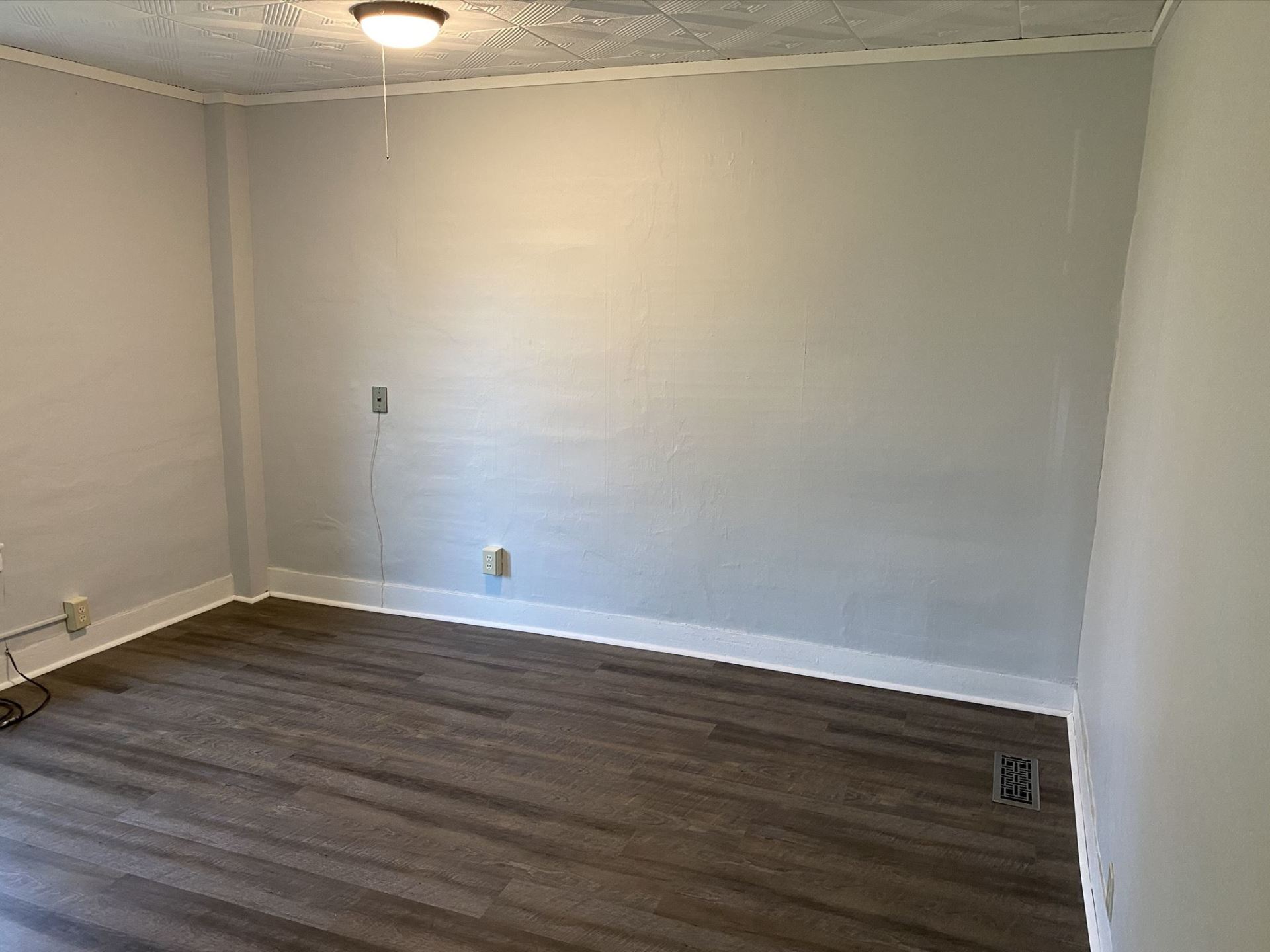 Empty room with gray walls, dark wood-look floor, and a ceiling light.