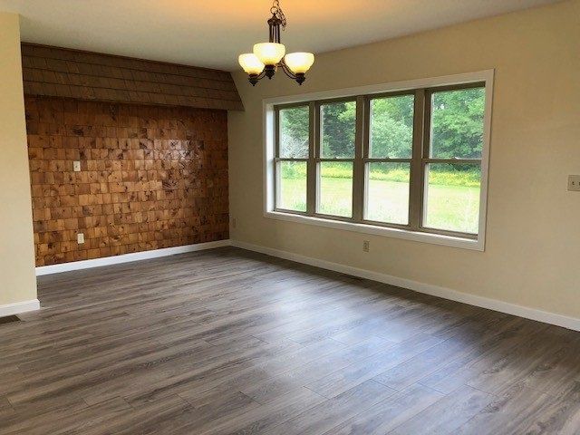 Empty dining room with wood accent wall and large window overlooking greenery. Gray flooring.