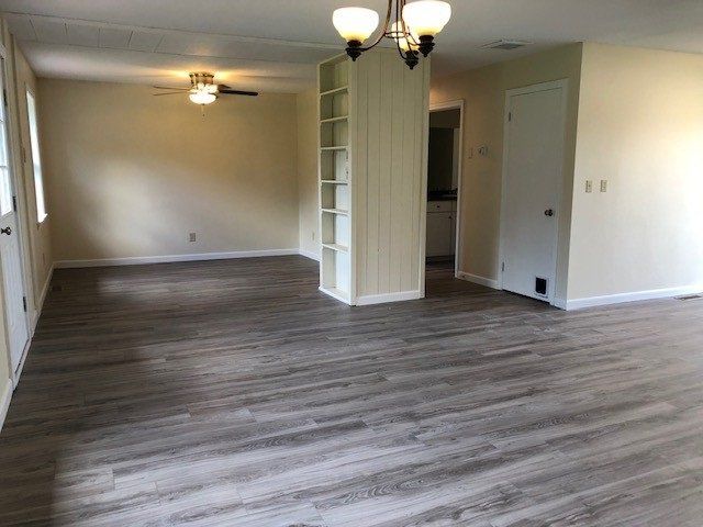 Empty living space with gray wood-look flooring, light walls, and a built-in bookcase.