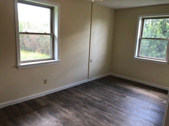 Empty room with two windows, wood-look flooring, and beige walls.