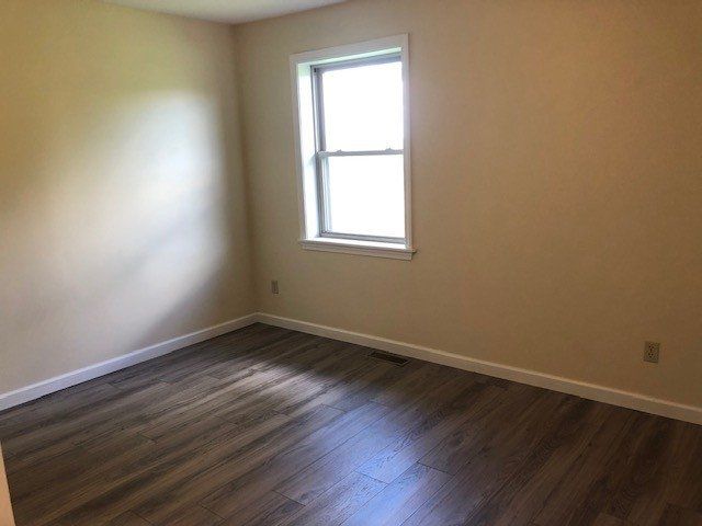 Empty room with wood-look flooring, tan walls, and a window.