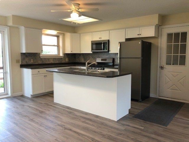 Modern kitchen with white cabinets, dark countertops, island, and stainless steel appliances.