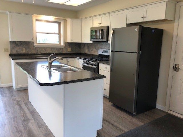 Kitchen with white cabinets, dark countertops, stainless steel appliances, and a gray island.