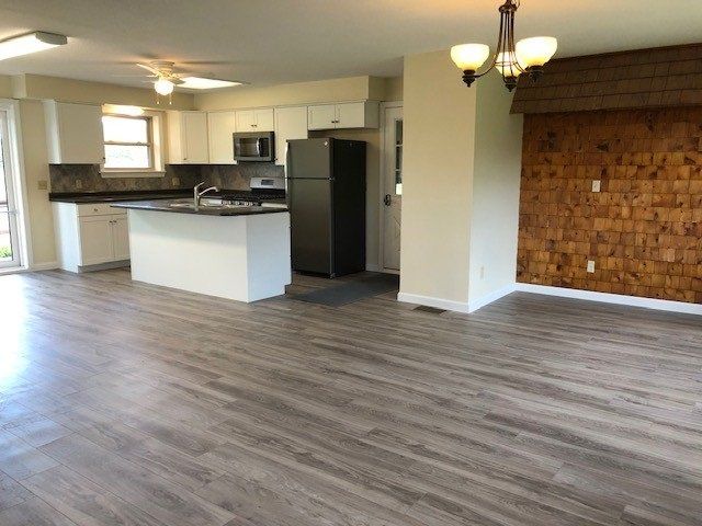 Open-concept kitchen and living area with wood-look flooring, white cabinetry, island, and a dark refrigerator.