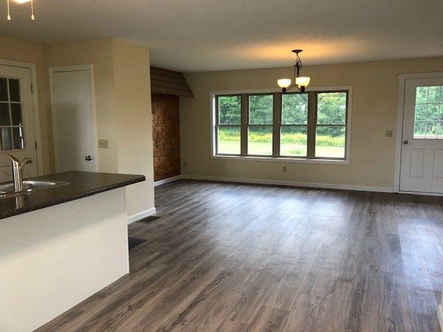 Interior view of a living space with gray flooring, large window, kitchen island, and white door.
