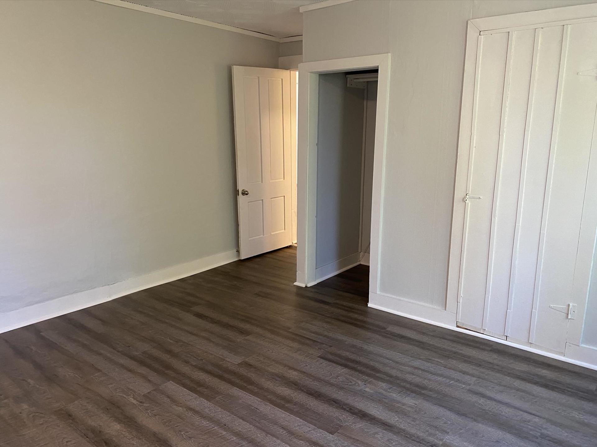 Empty room with gray walls, wood-look flooring, and a doorway.