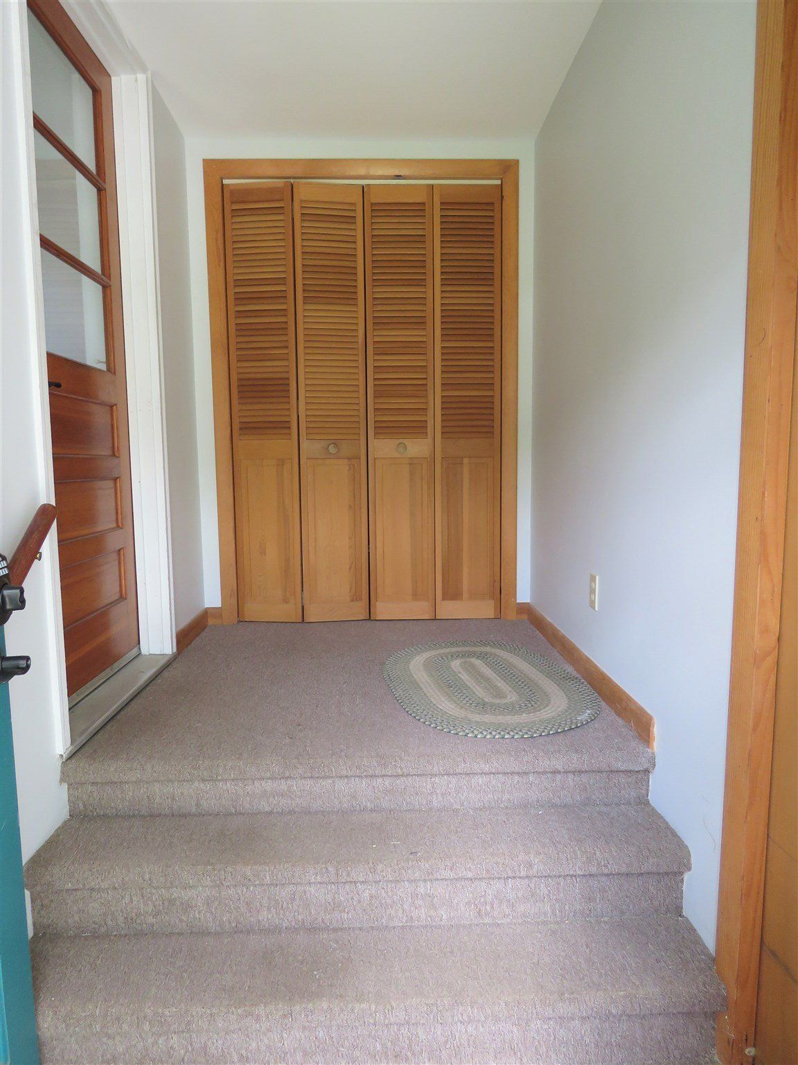 A hallway with stairs leading up to a closet with wooden shutters