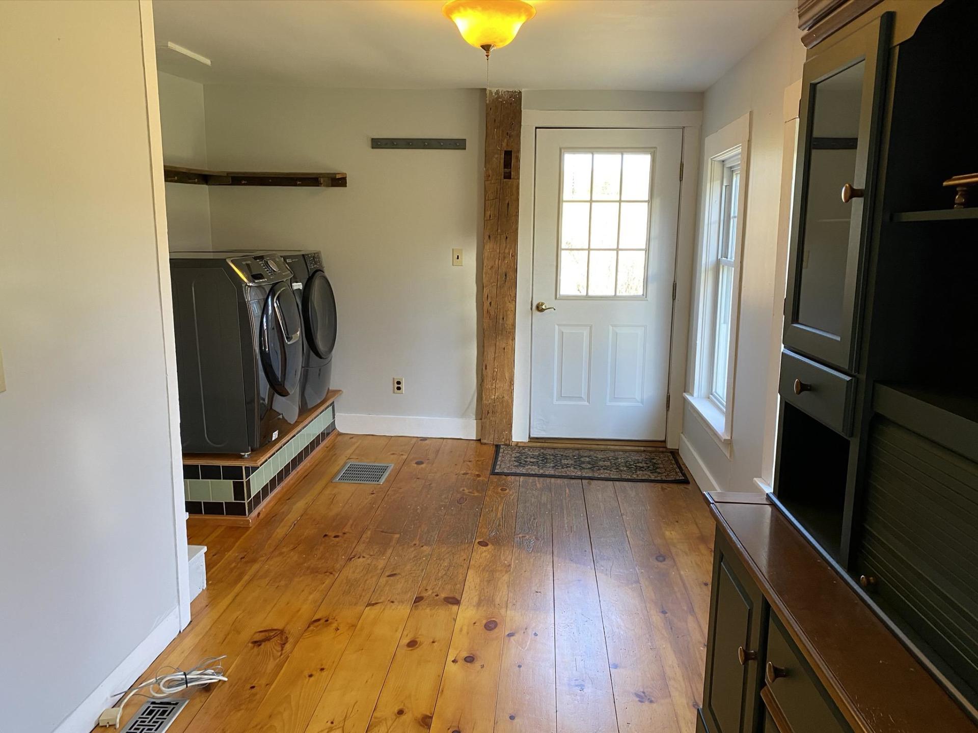 Hallway with wood floors, a door, and a black cabinet. Laundry machines are visible on the left.