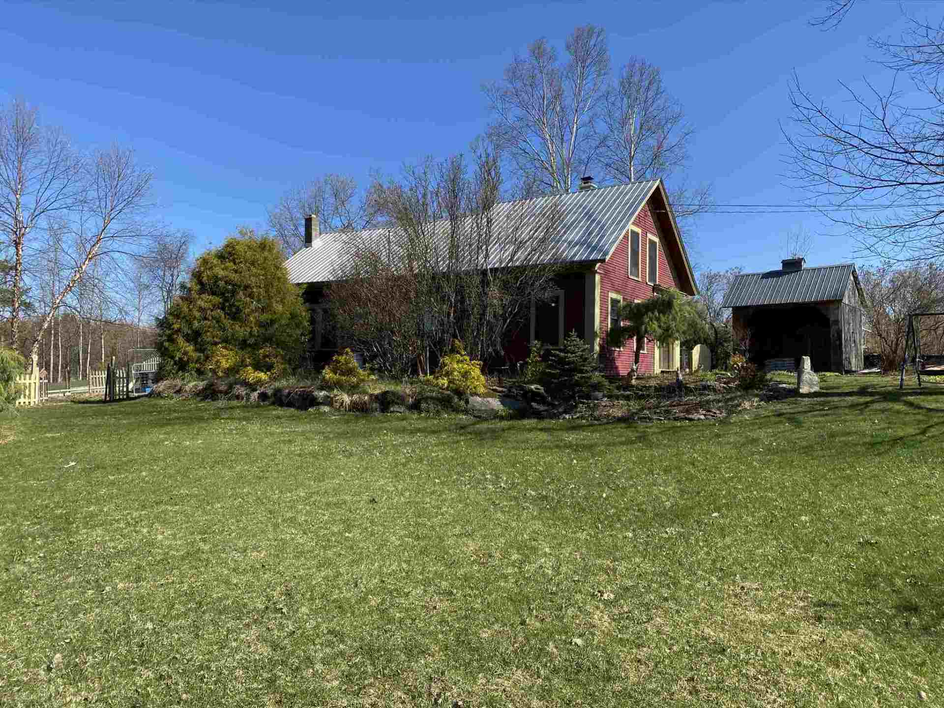 Red house with shed on a grassy lawn under a clear blue sky.