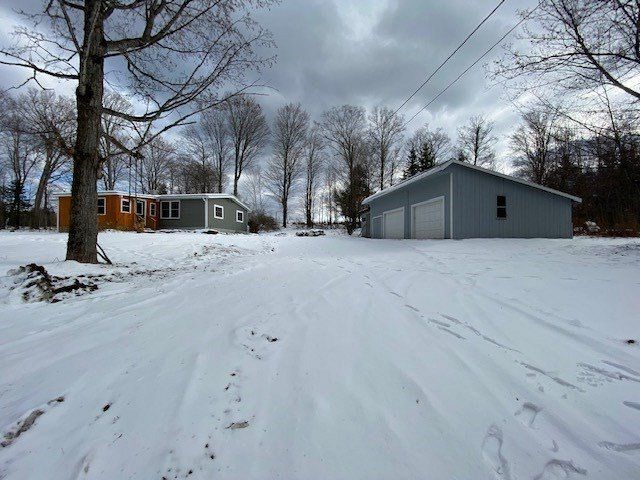 Snowy scene: houses and a garage on a snow-covered drive under a cloudy sky.