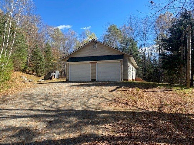 A garage with two garage doors is surrounded by trees and leaves