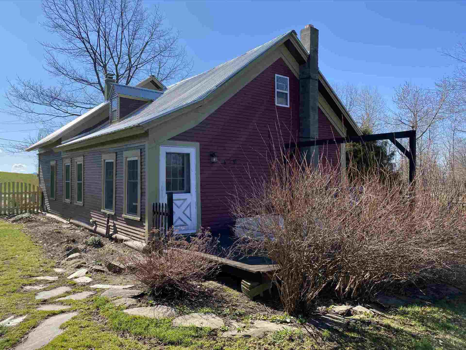 Red and brown house with white door, gray roof, and stone path on a sunny day.
