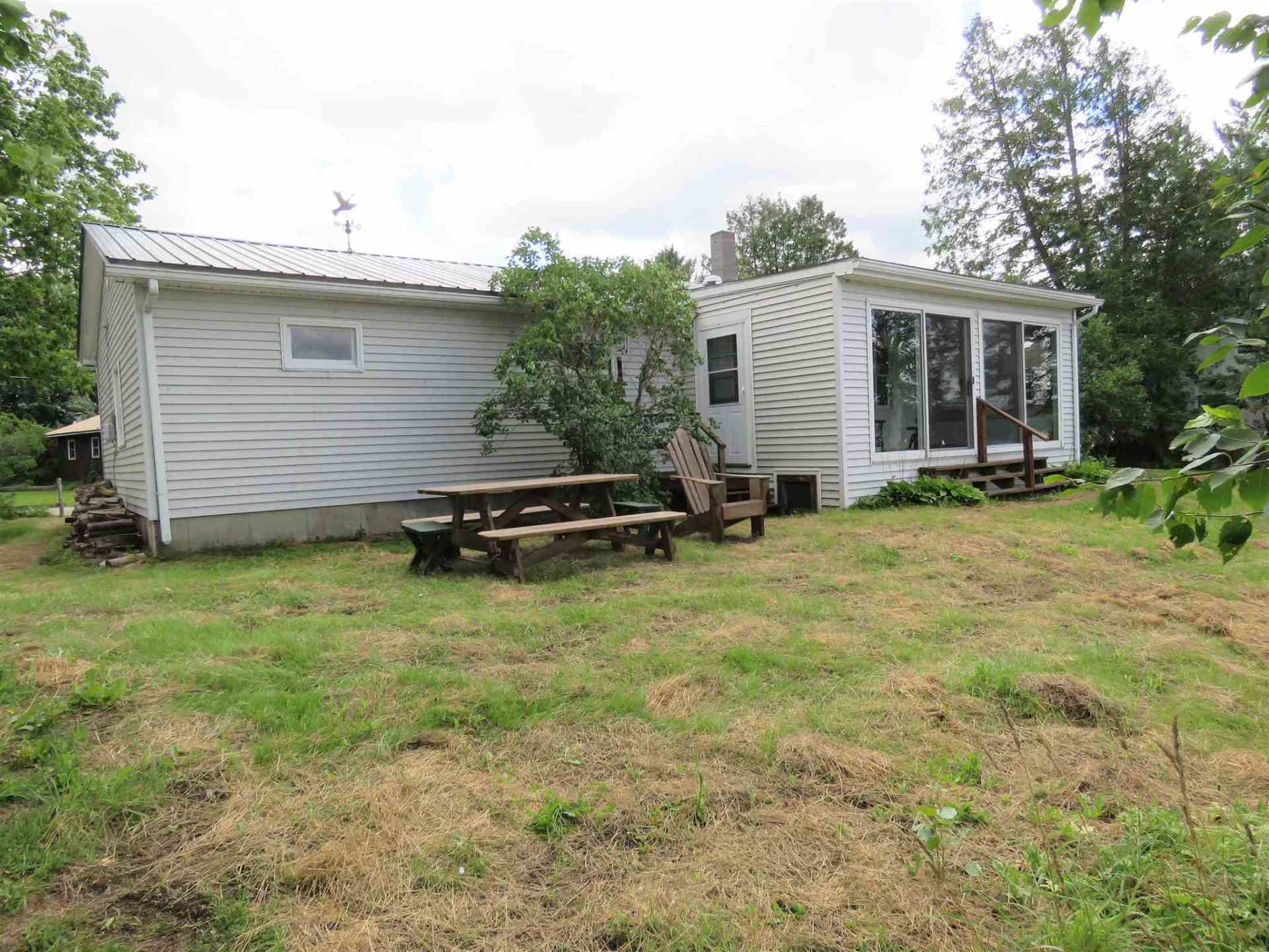 A small white house with a picnic table and chairs in front of it.
