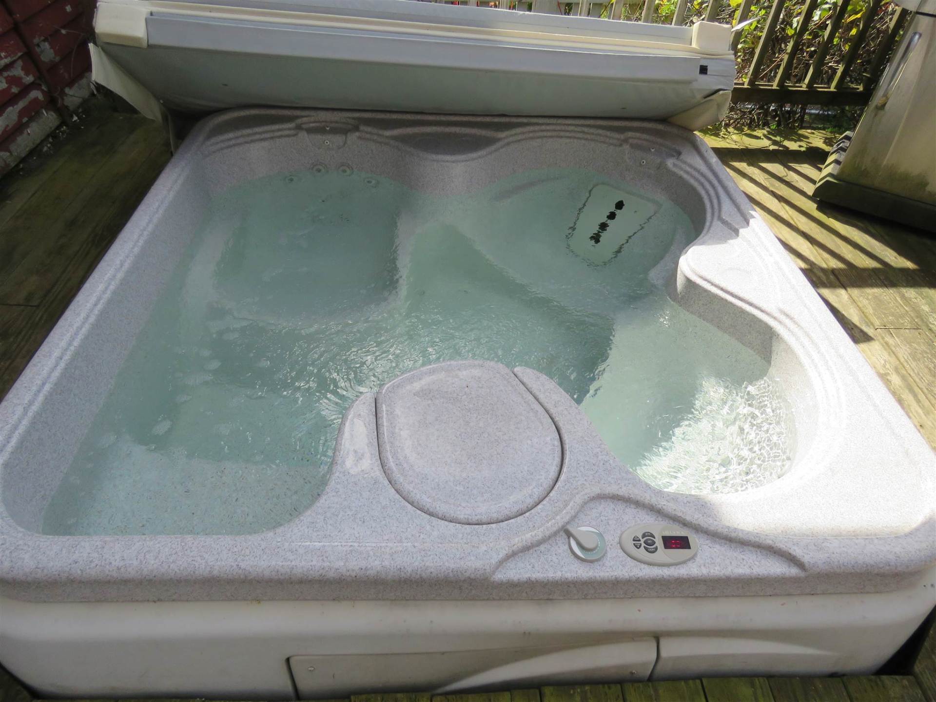Hot tub filled with water on a wooden deck, cover open.
