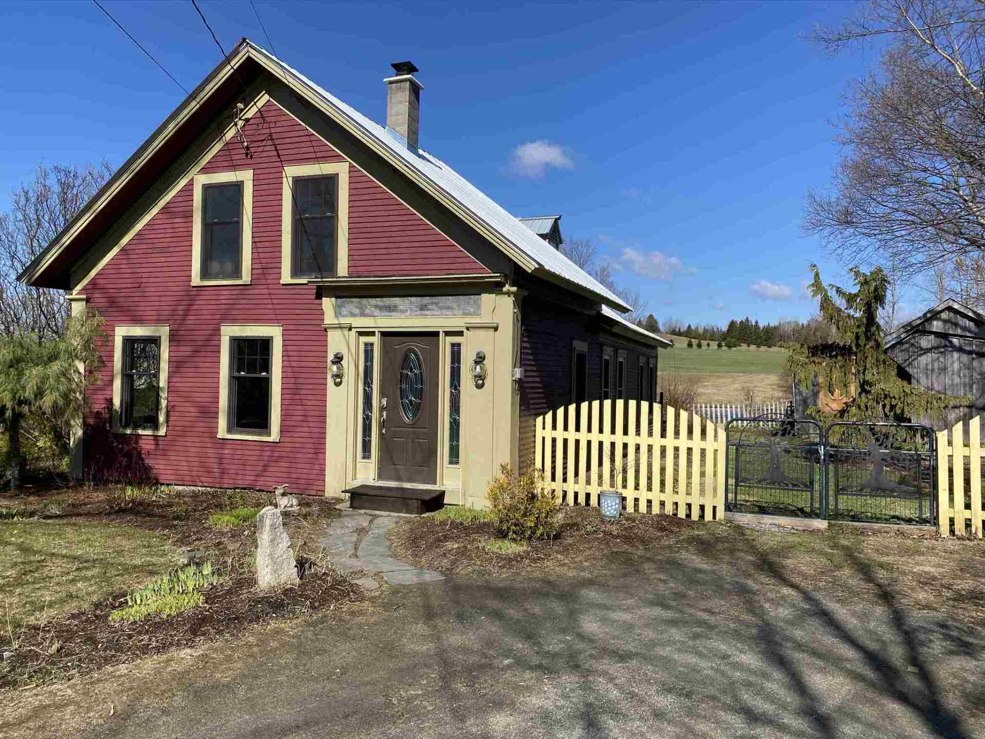 Red wooden house with yellow picket fence, blue sky.