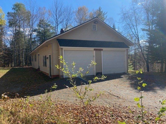 A garage with two garage doors is surrounded by trees and leaves.