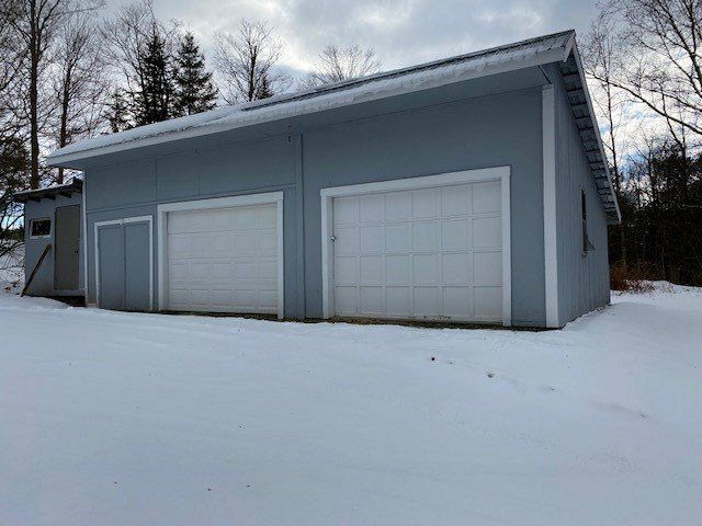 A light blue garage with two white garage doors, in a snowy setting.