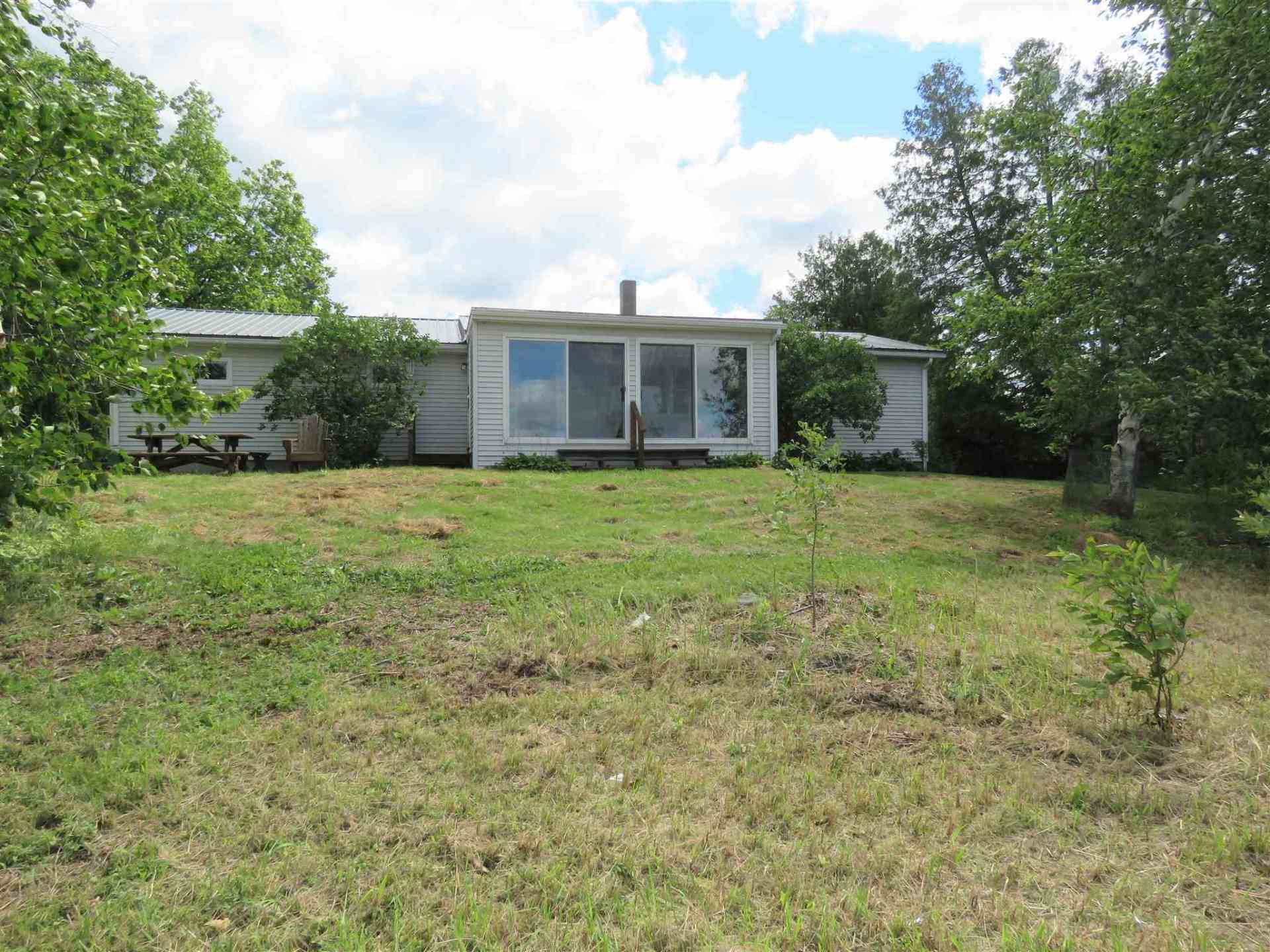 A small white house sits in the middle of a grassy field