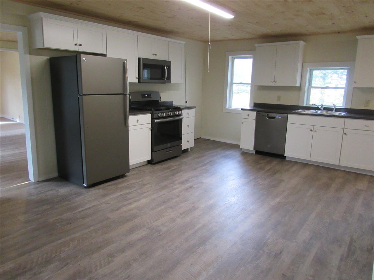 Empty kitchen with white cabinets, stainless steel appliances, and dark wood-look flooring.