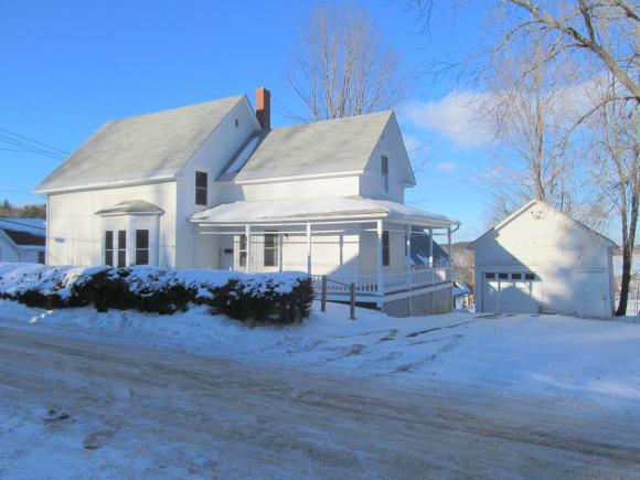 White house with snow-covered lawn and driveway, small porch, detached garage; bright, sunny winter day.