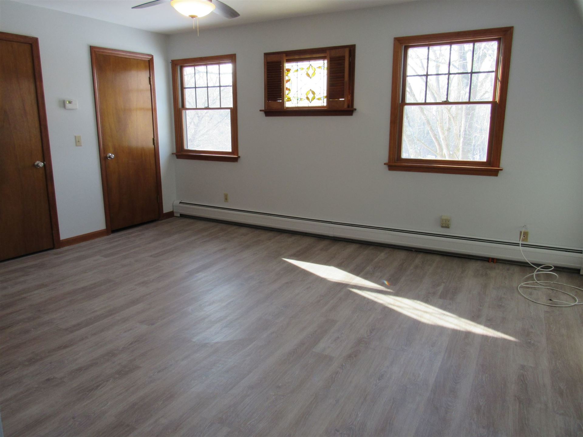 An empty room with a ceiling fan and three windows
