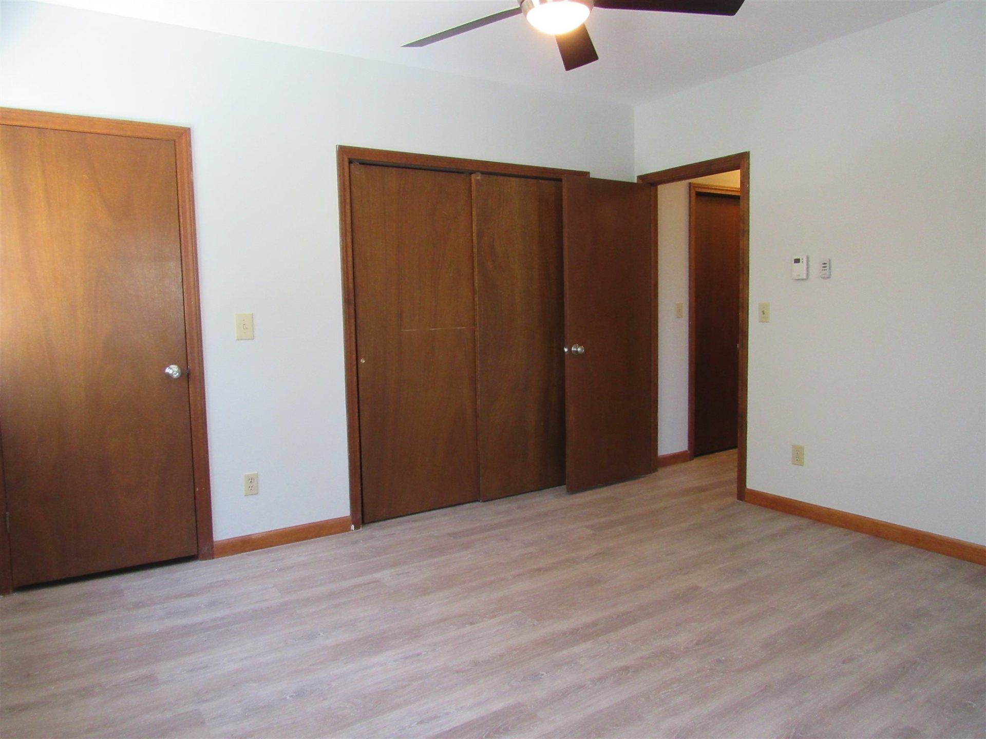 An empty bedroom with wooden doors and a ceiling fan