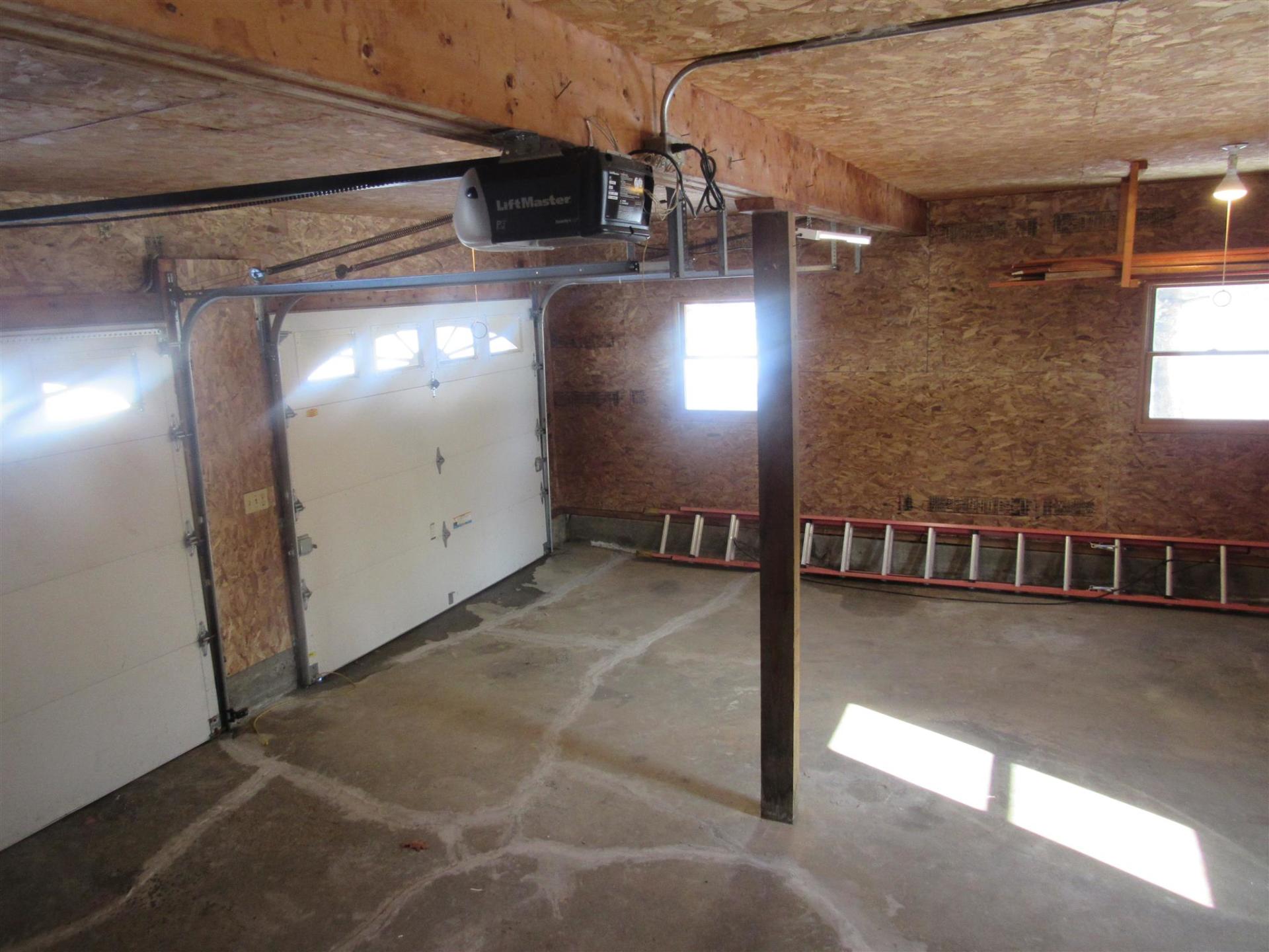 Interior of a garage with a closed garage door. There is a support beam, ladders, and two windows.