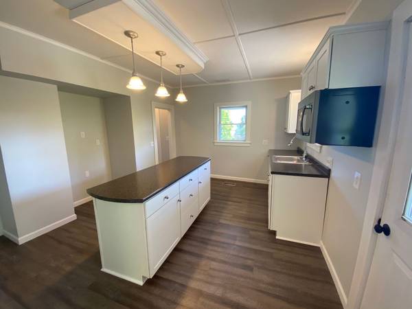 Modern kitchen with white cabinets, dark countertops, island, and wood-look flooring.