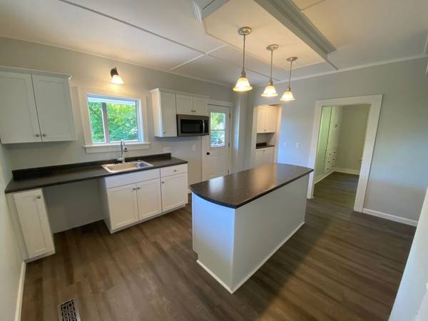White kitchen with dark countertops and island; three hanging lights.