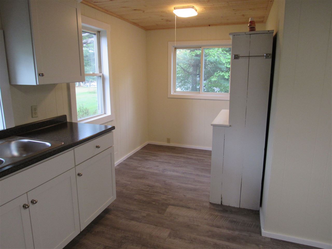 Small kitchen with white cabinets, dark countertop, and wood-look flooring. Light coming in from a window.