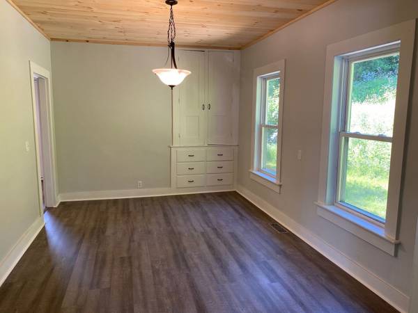 Empty dining room with wood ceiling and floors, built-in cabinets, and two windows.