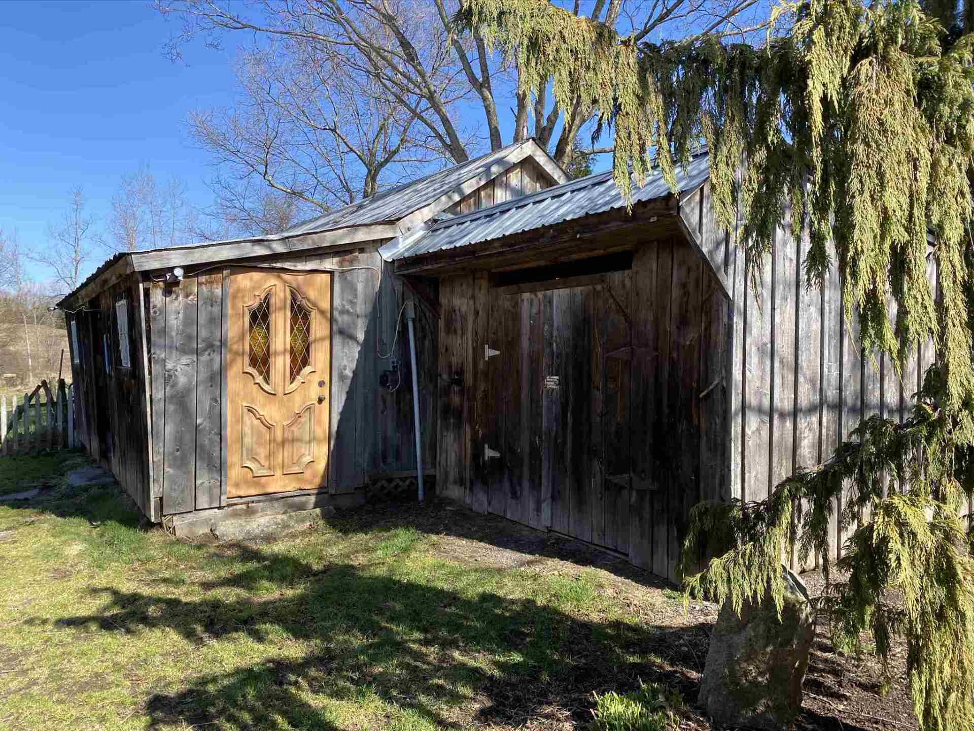 Old wooden shed with two doors, weathered wood, metal roof, on grassy ground.