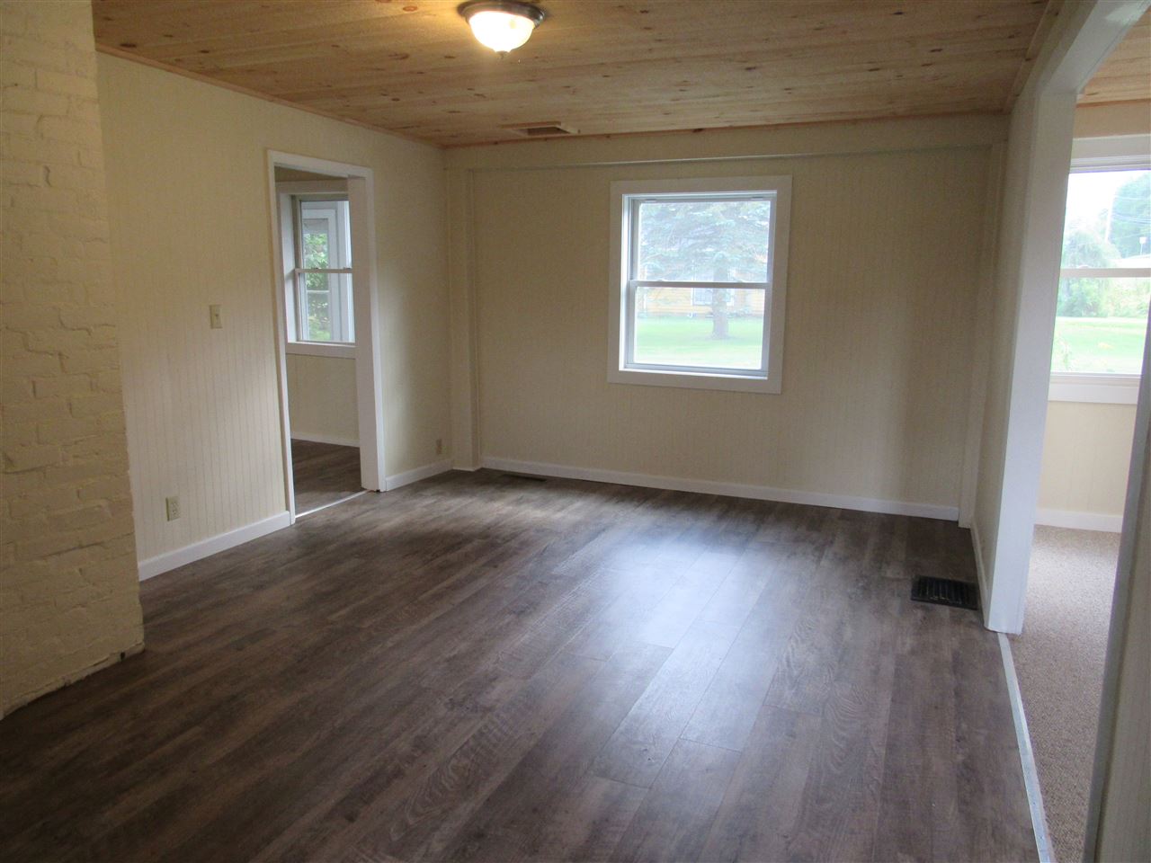 Empty living room with wood floor, window, and wood-paneled ceiling.