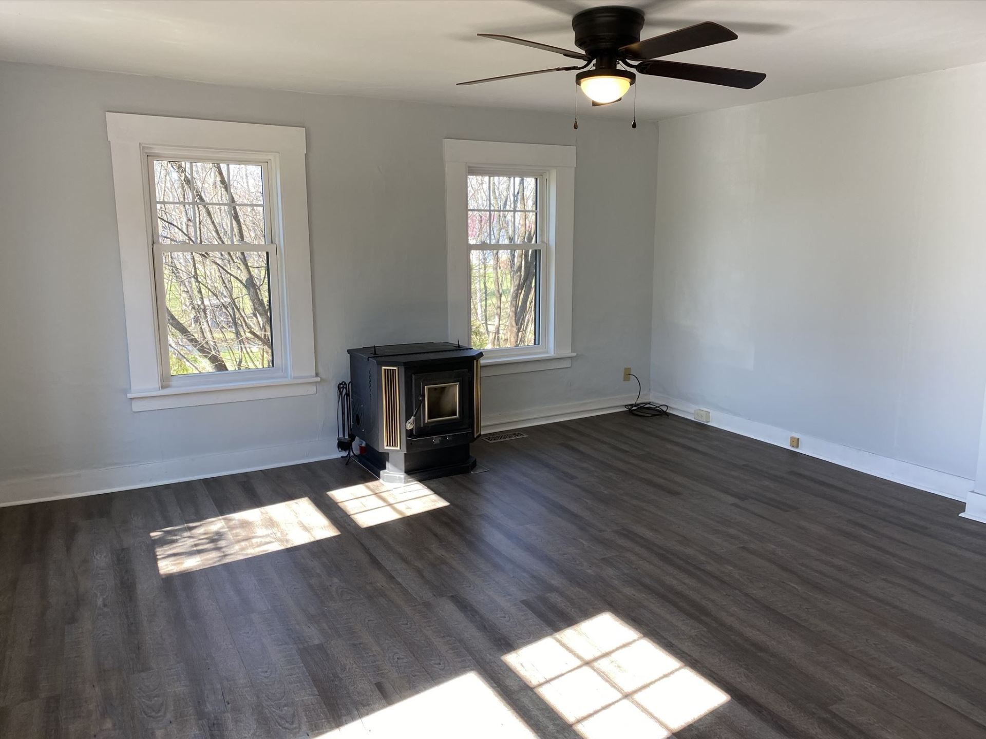 Empty room with gray flooring, two windows, a black stove, and a ceiling fan.