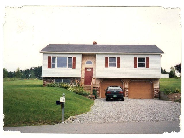 Suburban house with white siding, red shutters, a car in the driveway, and a mailbox by the road