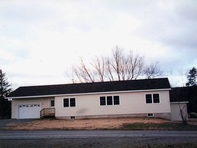 Single-story beige house with attached garage and dark roof on a quiet street