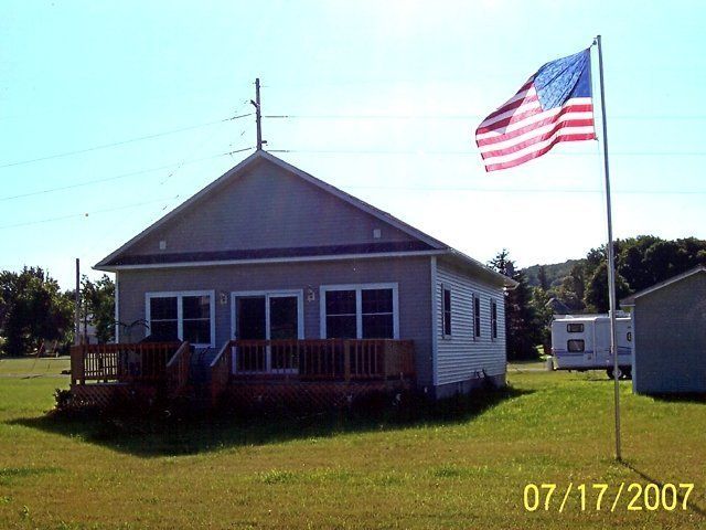 Small white house with a front porch and a large American flag on a sunny lawn.