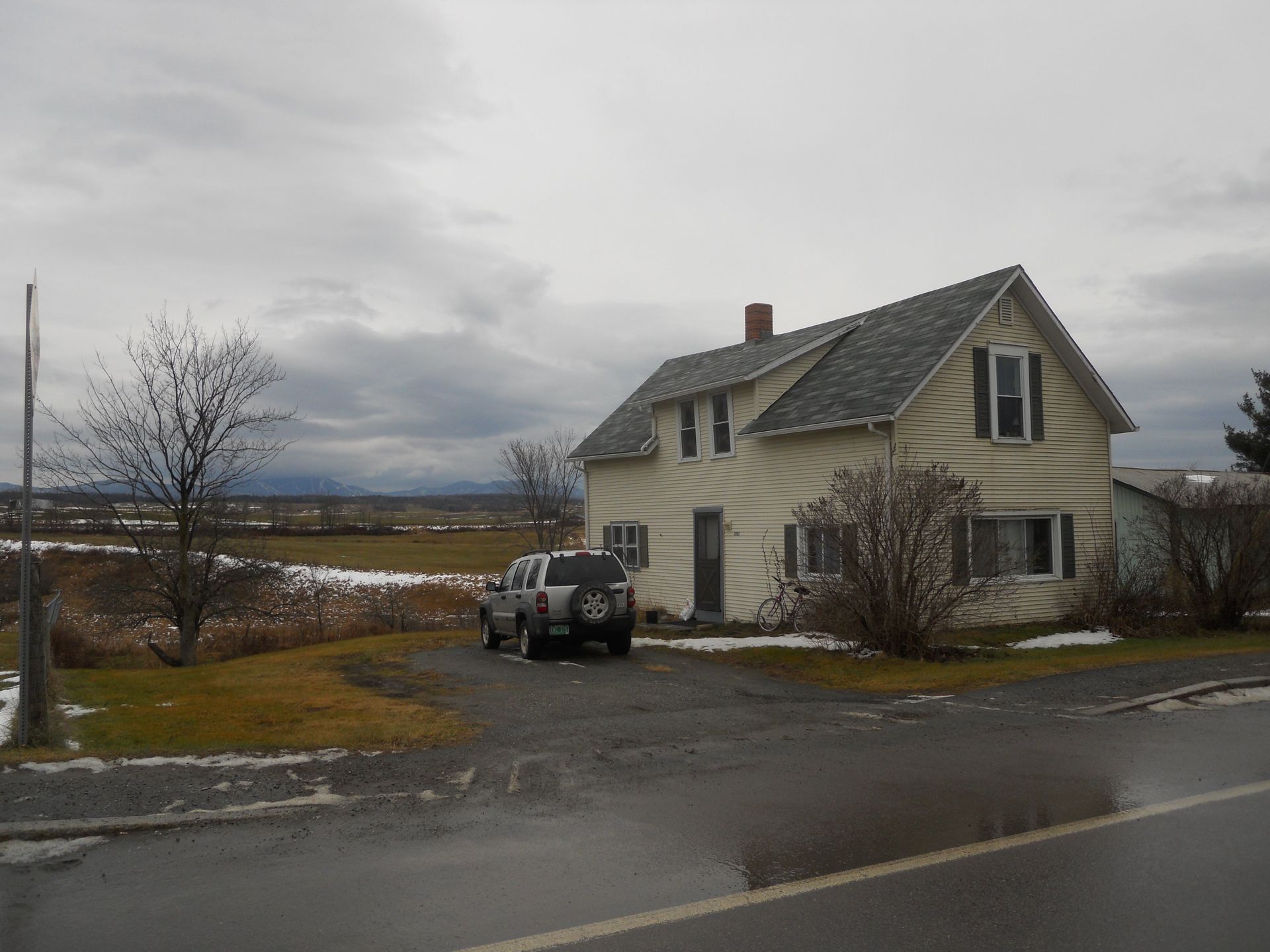 Two-story cream-colored house on a cloudy day, SUV parked in front.