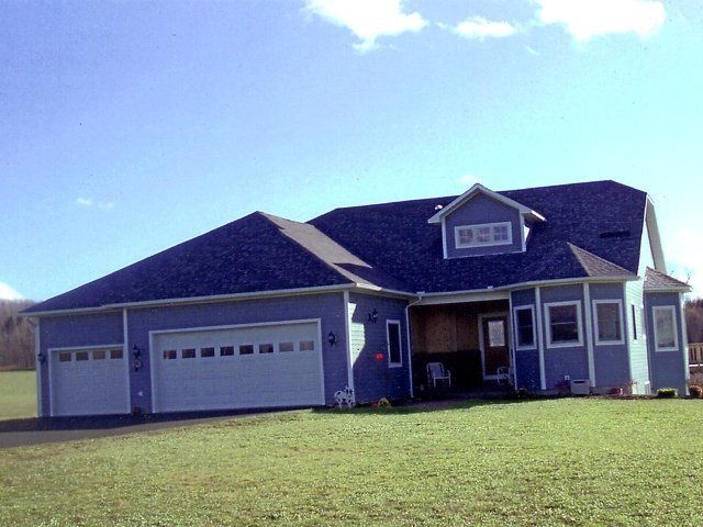 Single-story suburban house with blue siding, two garage doors, and a large front lawn under a clear sky