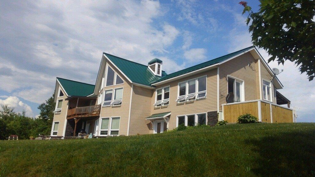 Large tan house with green roofs on a grassy hill under a cloudy sky