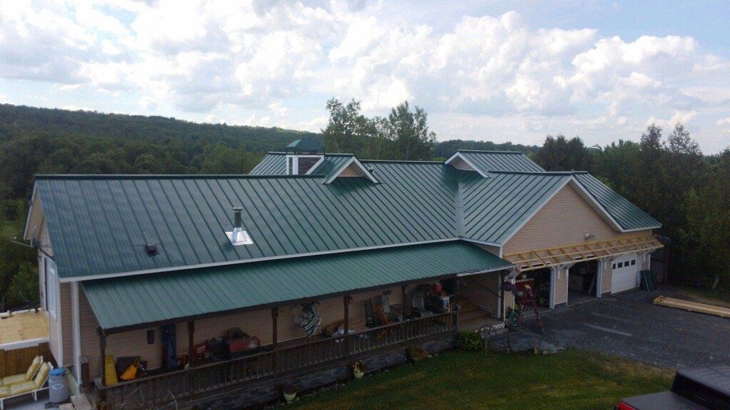 Rural house with green metal roof, front porch, and garage under a cloudy sky