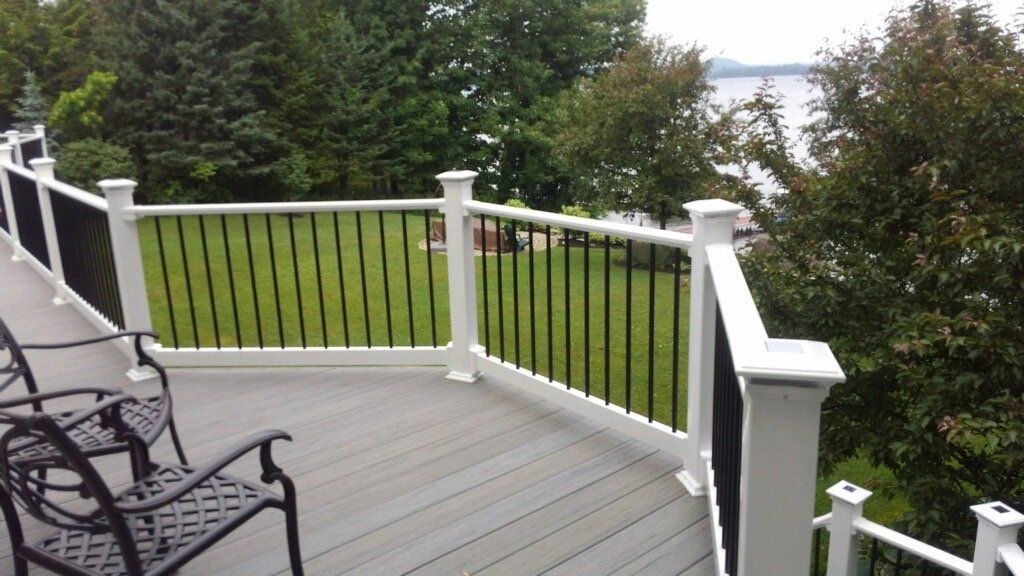 Wooden deck with white railing overlooking trees and water, with a black metal bench in the corner