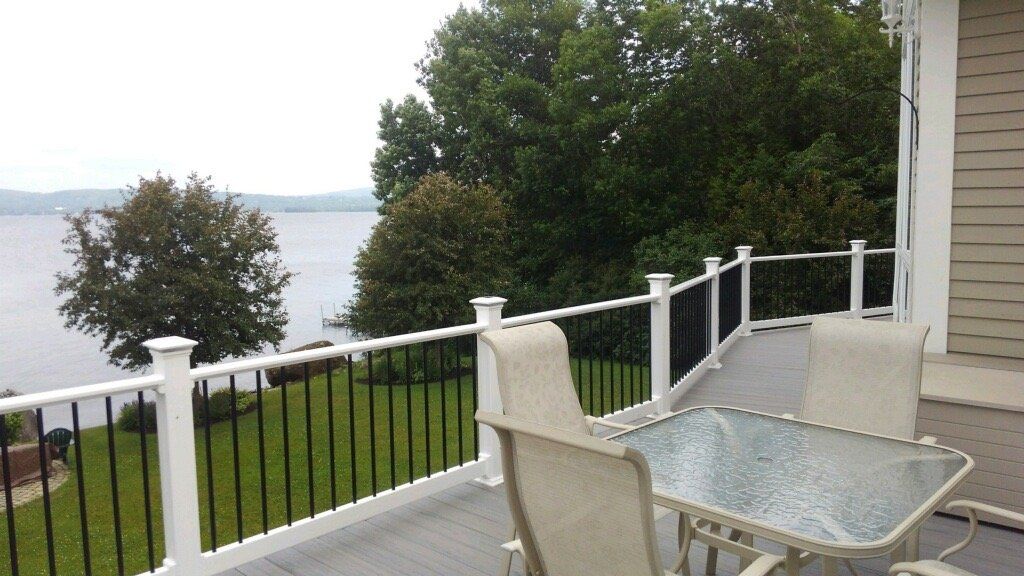 Patio with glass table and chairs overlooking a lake and trees from a house deck